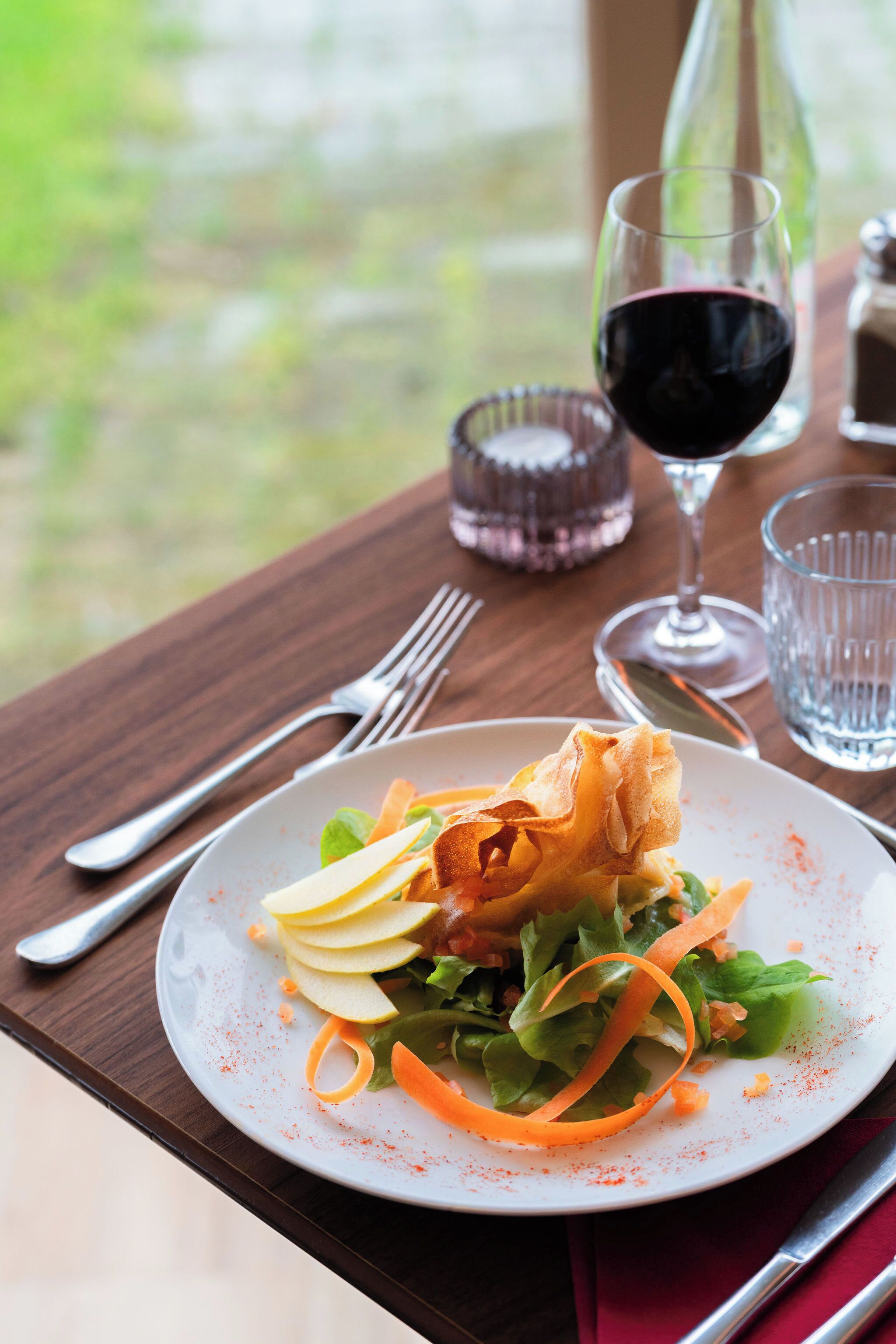 Un plato de comida con ensalada, una copa de vino y un vaso de agua sobre una mesa de madera.