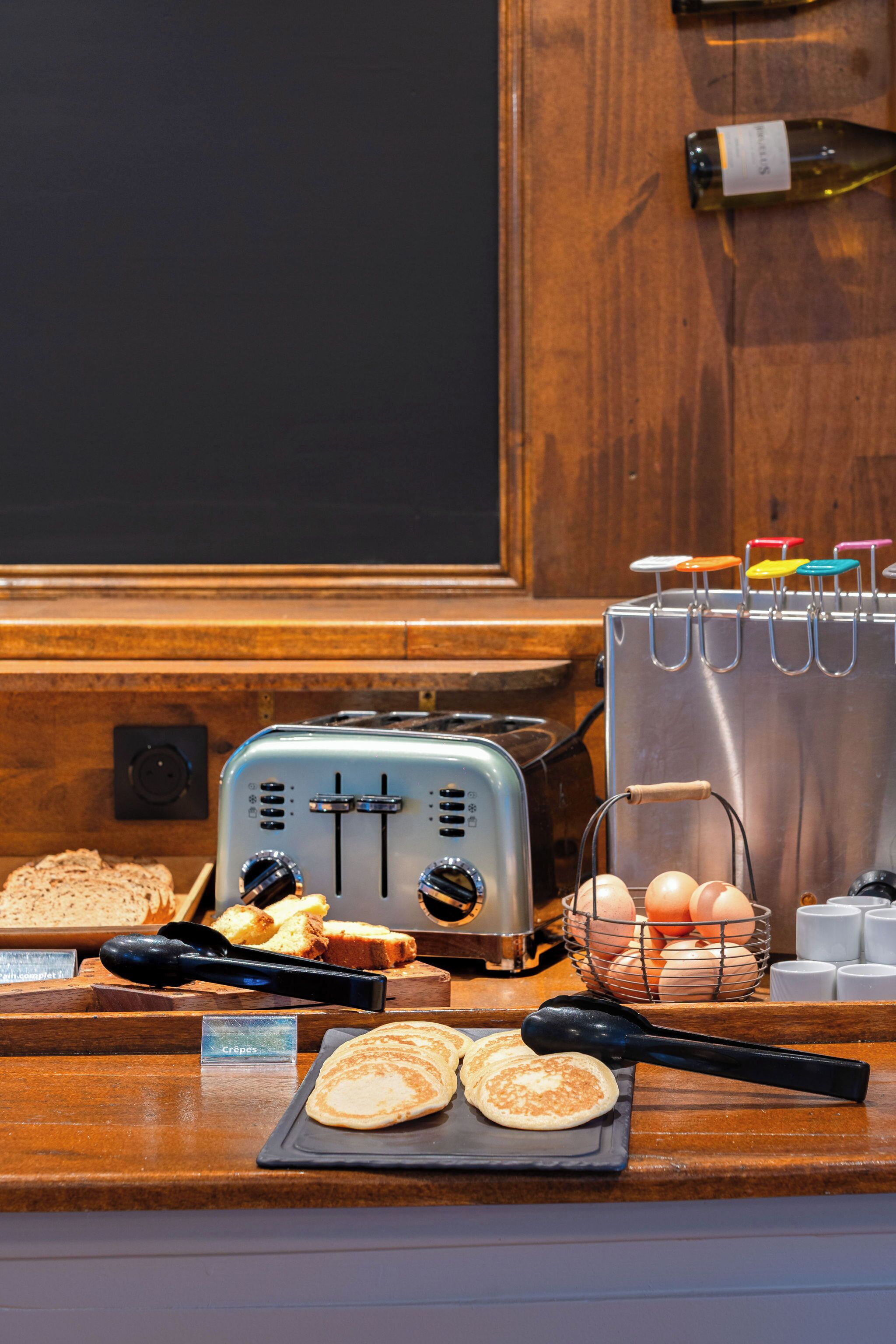 Een ontbijtbuffet met een broodrooster, brood, eieren en een bordje met de tekst 'Crepes'.