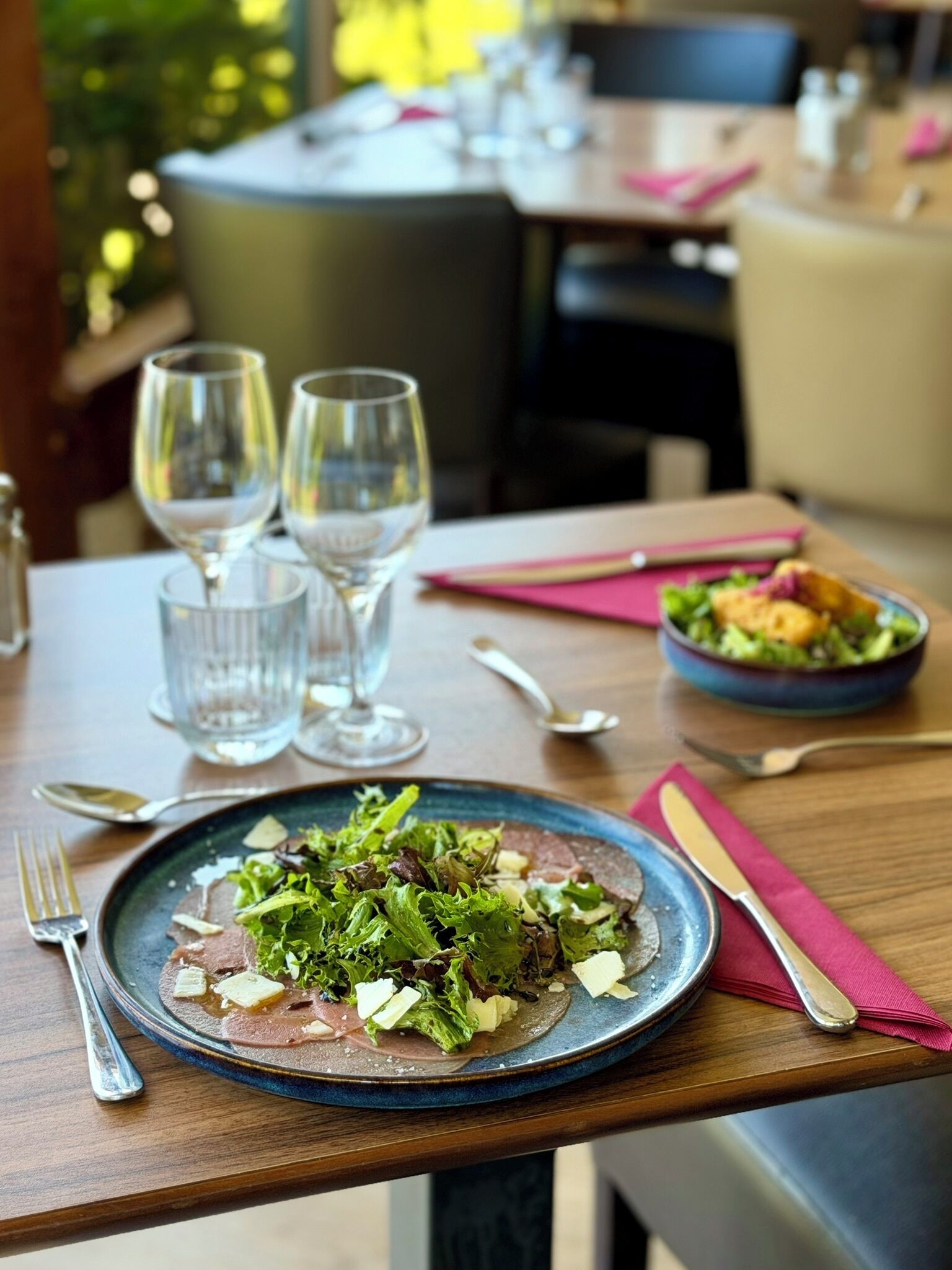 Ein Esstisch mit einer Schüssel Essen, zwei Weingläsern und einer Salatschüssel.