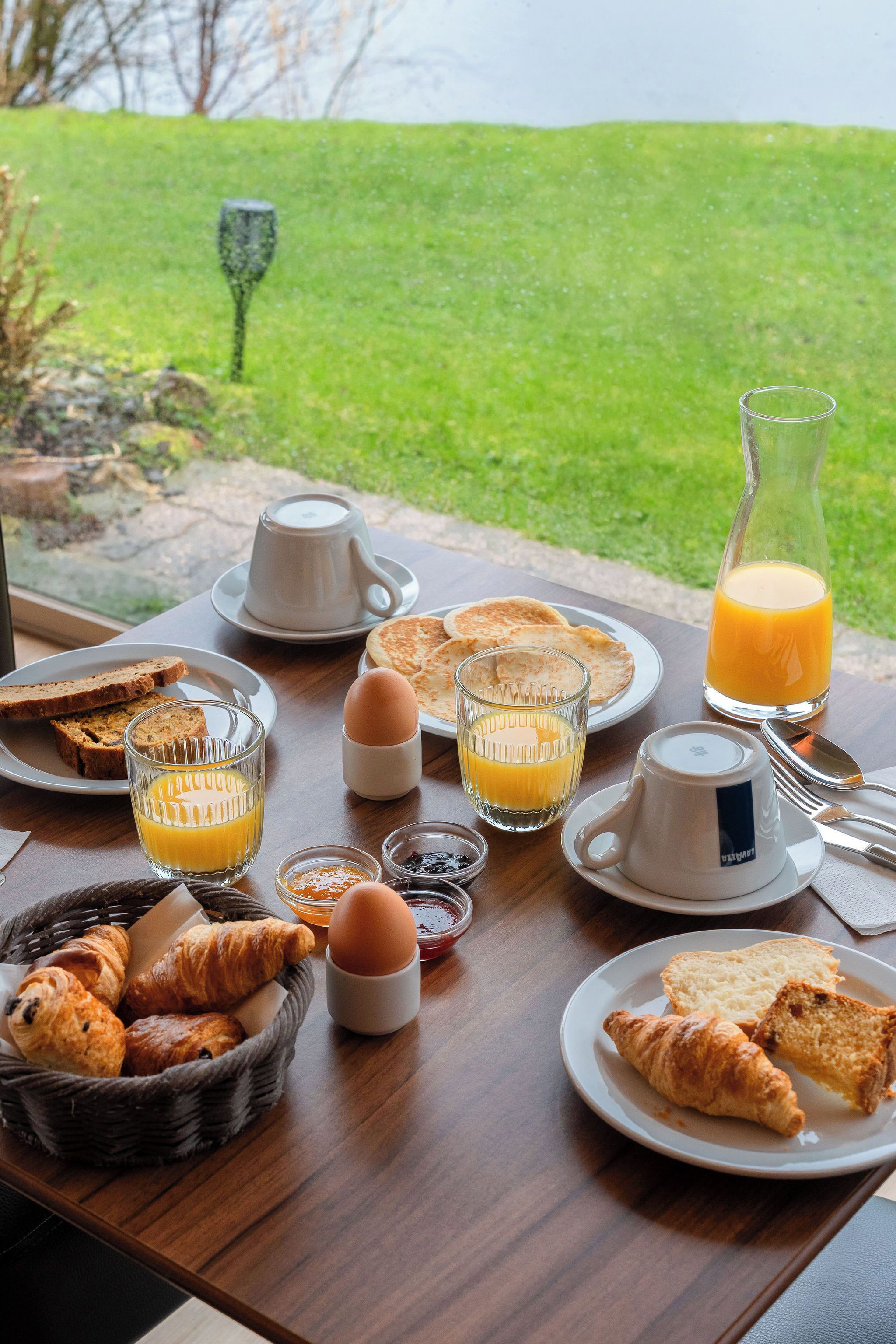 A breakfast table with croissants, toast, eggs, juice, and a pitcher of orange juice.