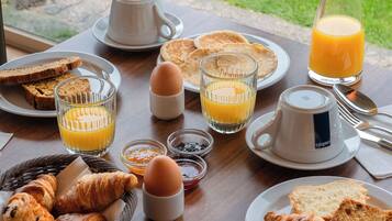 A breakfast table with croissants, toast, eggs, juice, and a pitcher of orange juice.