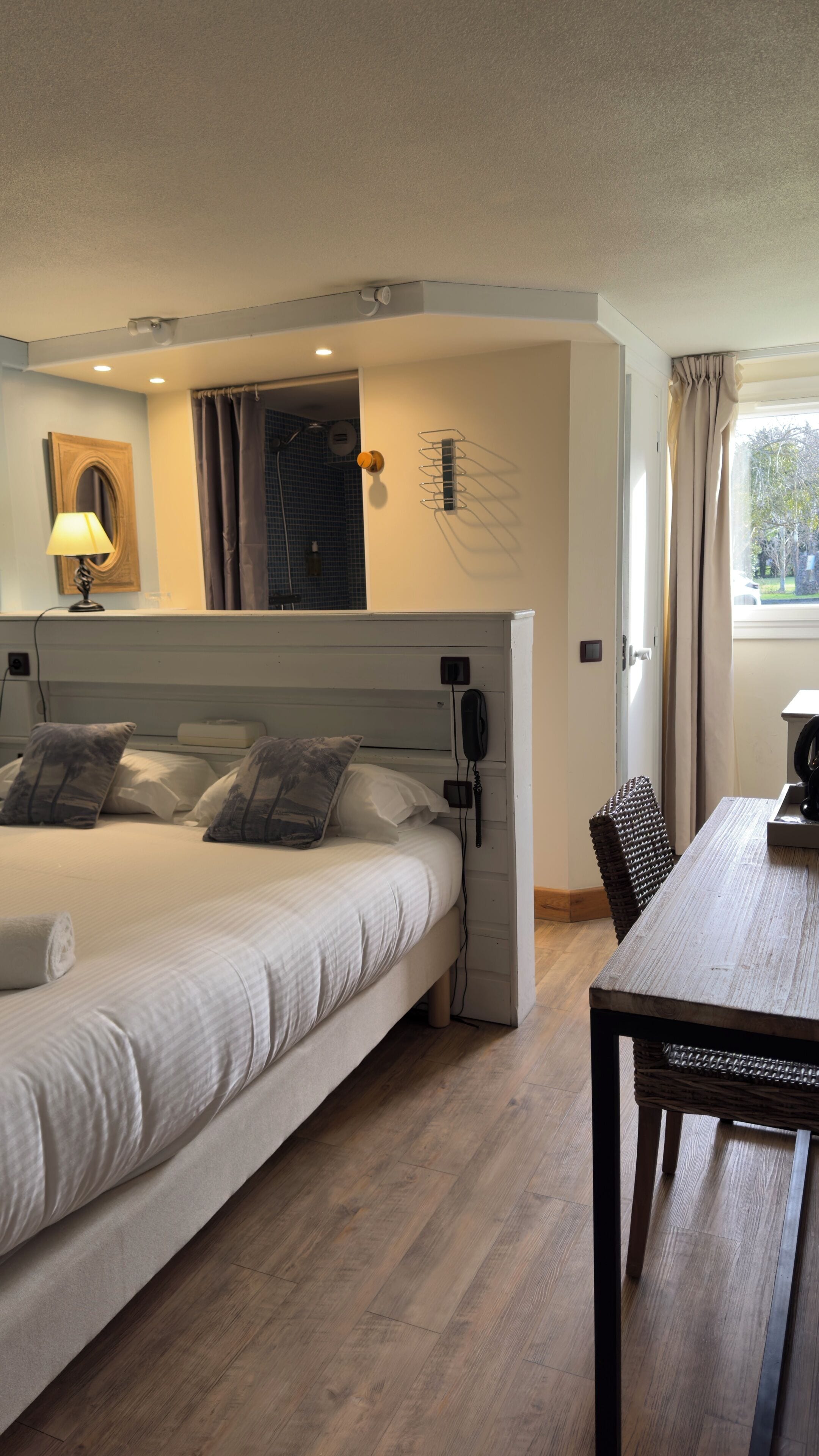 A hotel room with a bed, bedside table, and a view of the outdoors.