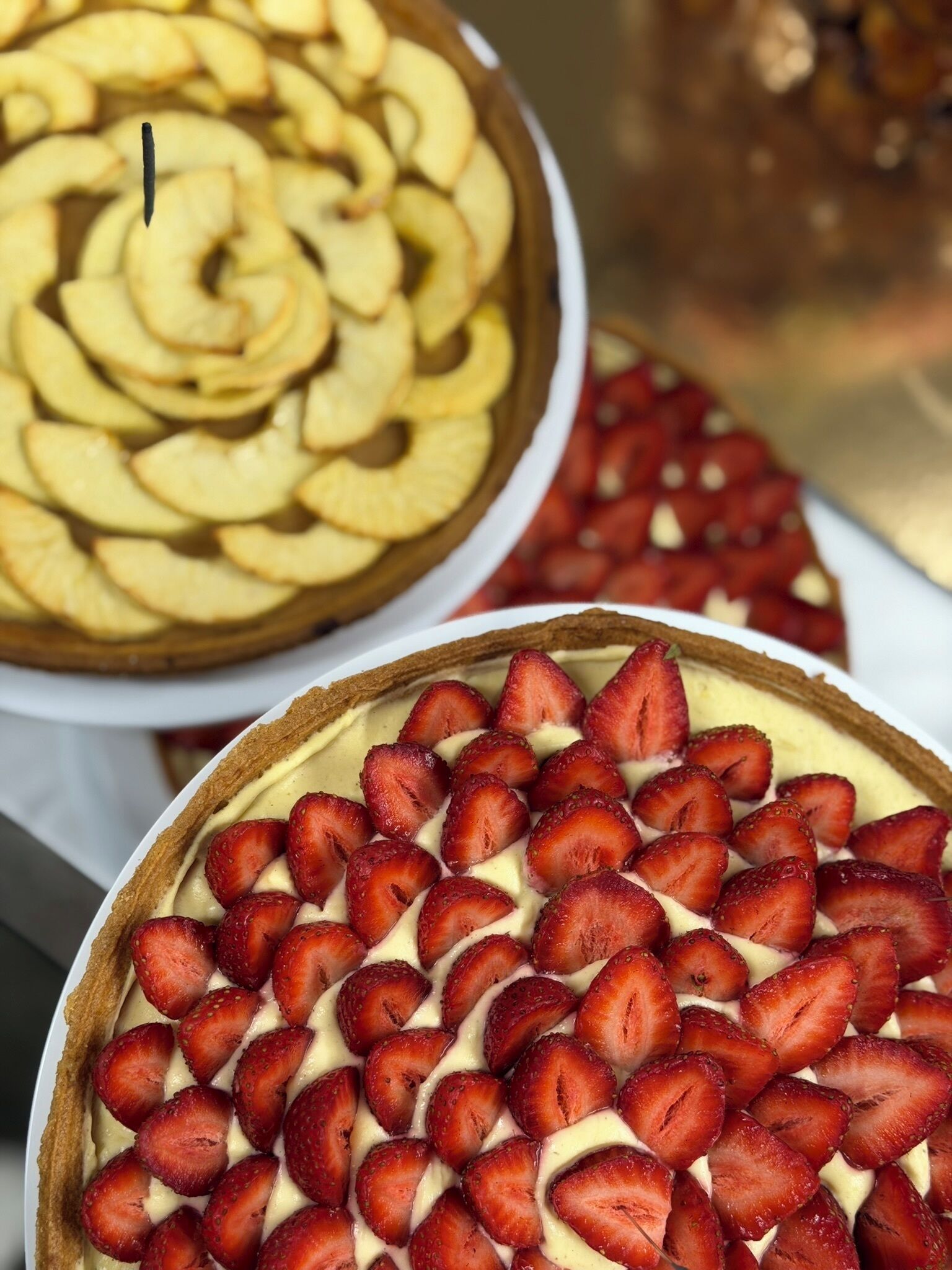 Une présentation de desserts comprenant une tarte garnie de fraises en tranches et une autre, avec des tranches de pommes.