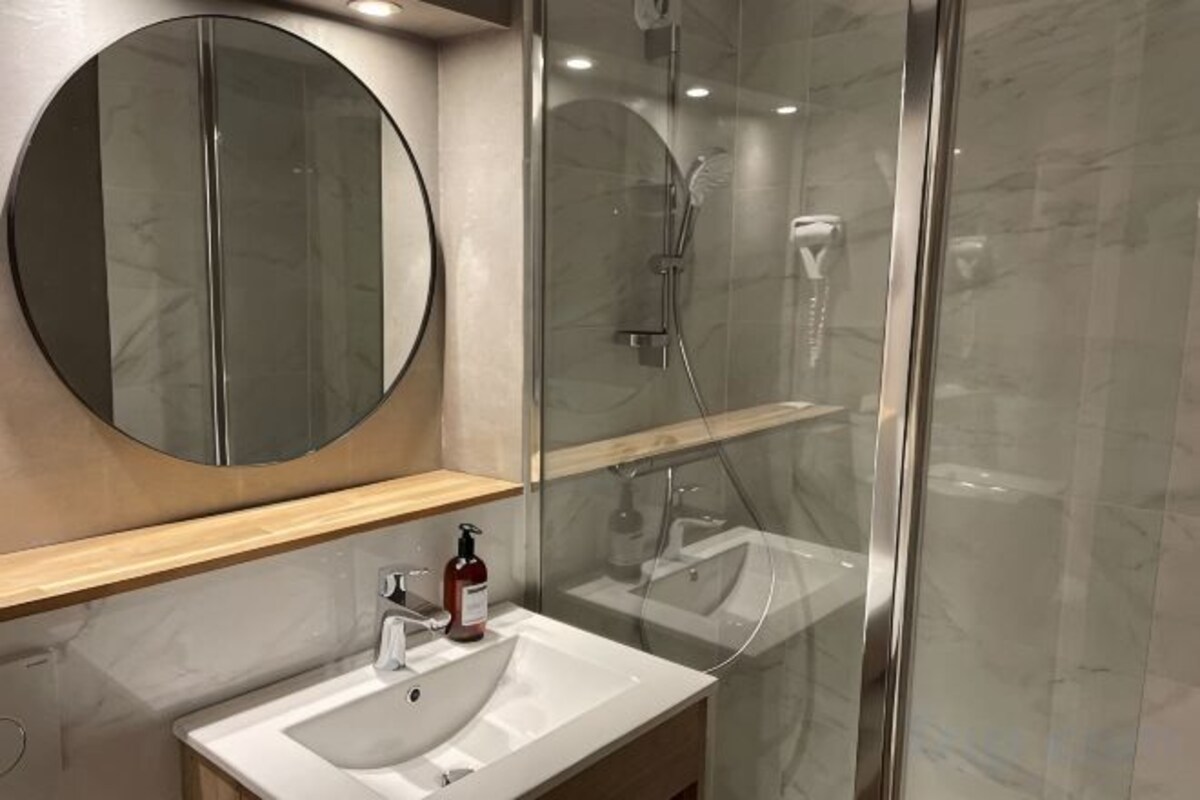 A modern bathroom with a round mirror, a white sink, and a glass-enclosed shower area.