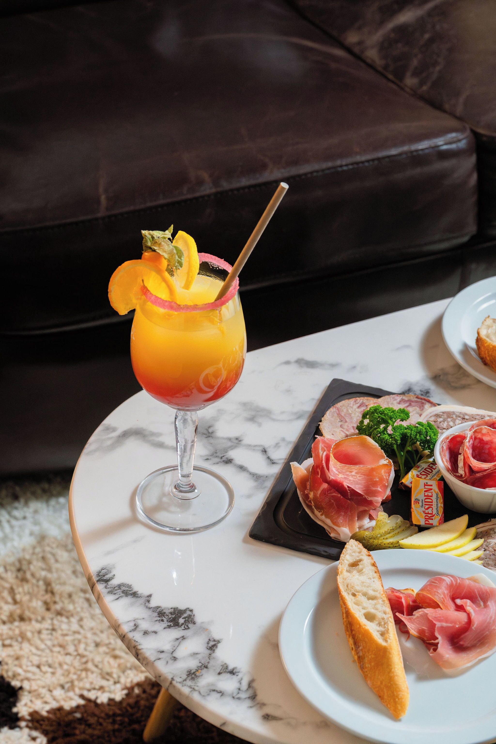 A table with a glass of orange juice, a plate of prosciutto, and a slice of bread.
