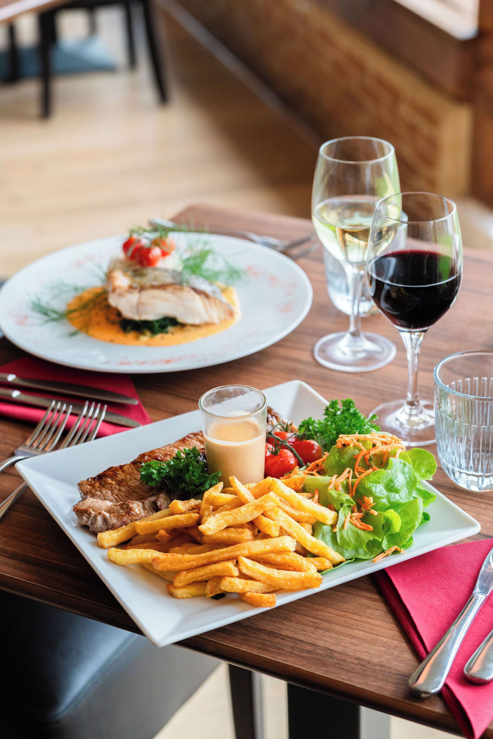 Une table à manger avec une assiette de steak et de frites, une salade et deux verres de vin.