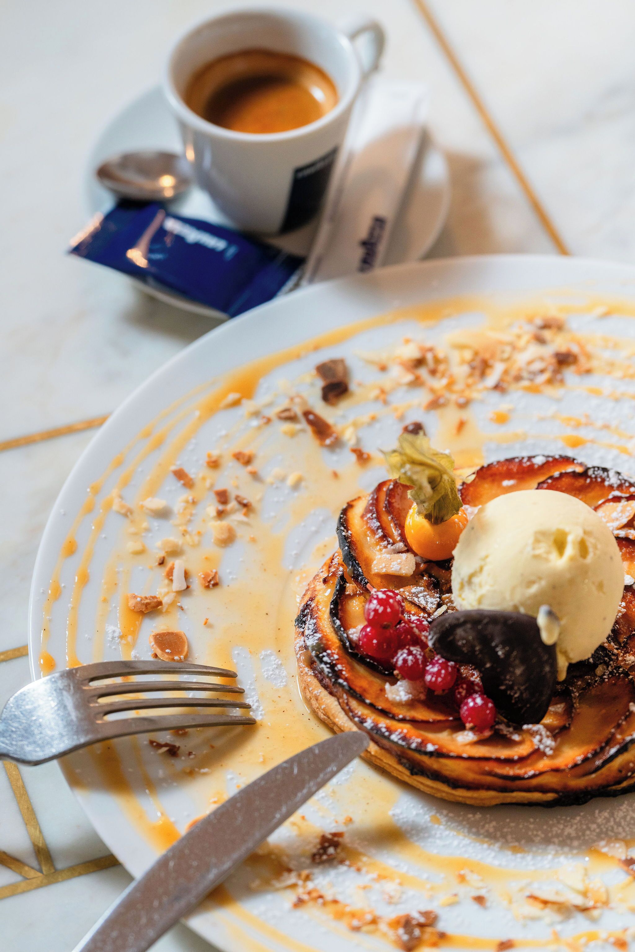 Prato de sobremesa com um doce, sorvete e frutas vermelhas, acompanhado de uma xícara de café e uma colher.