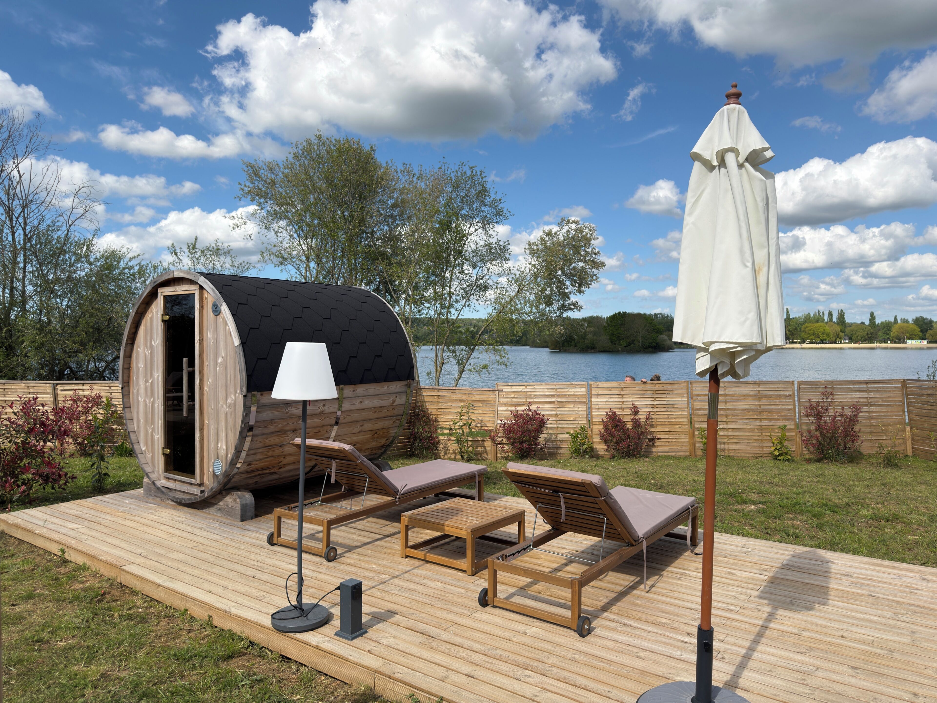 A wooden deck with a sauna, lounge chairs, and a table.