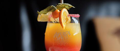 A cocktail in a stemmed glass with a straw, garnished with an orange slice and a green leaf, on a marble surface.