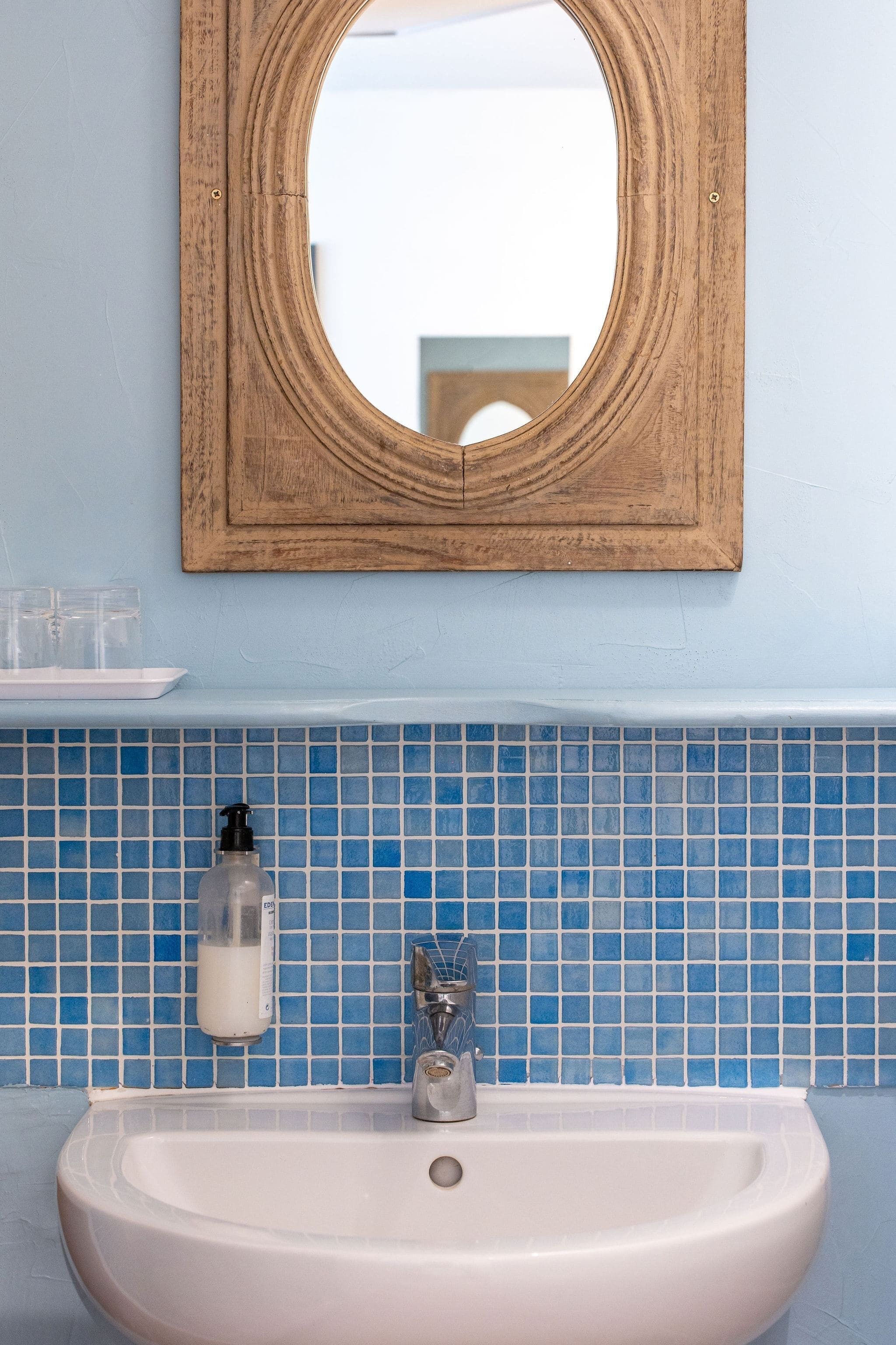 Une salle de bain avec un lavabo blanc, un miroir avec un cadre en bois et des murs recouverts de carreaux bleus.