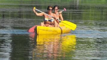 A yellow raft with two people paddling on a calm lake surrounded by greenery.