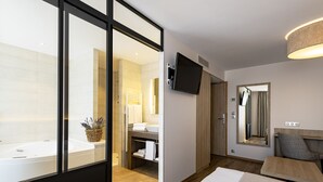 Un baño moderno con bañera, ducha y lavamanos. Hay un televisor montado en la pared y un espejo sobre el lavamanos.