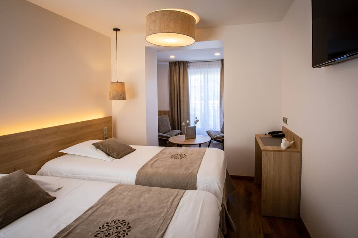 A hotel room with two beds, a desk, a chair, a television, and a window with curtains.
