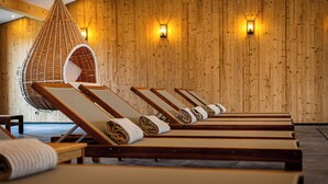 Una hilera de sillones de madera con toallas, una silla colgante e iluminación empotrada en una habitación de madera.