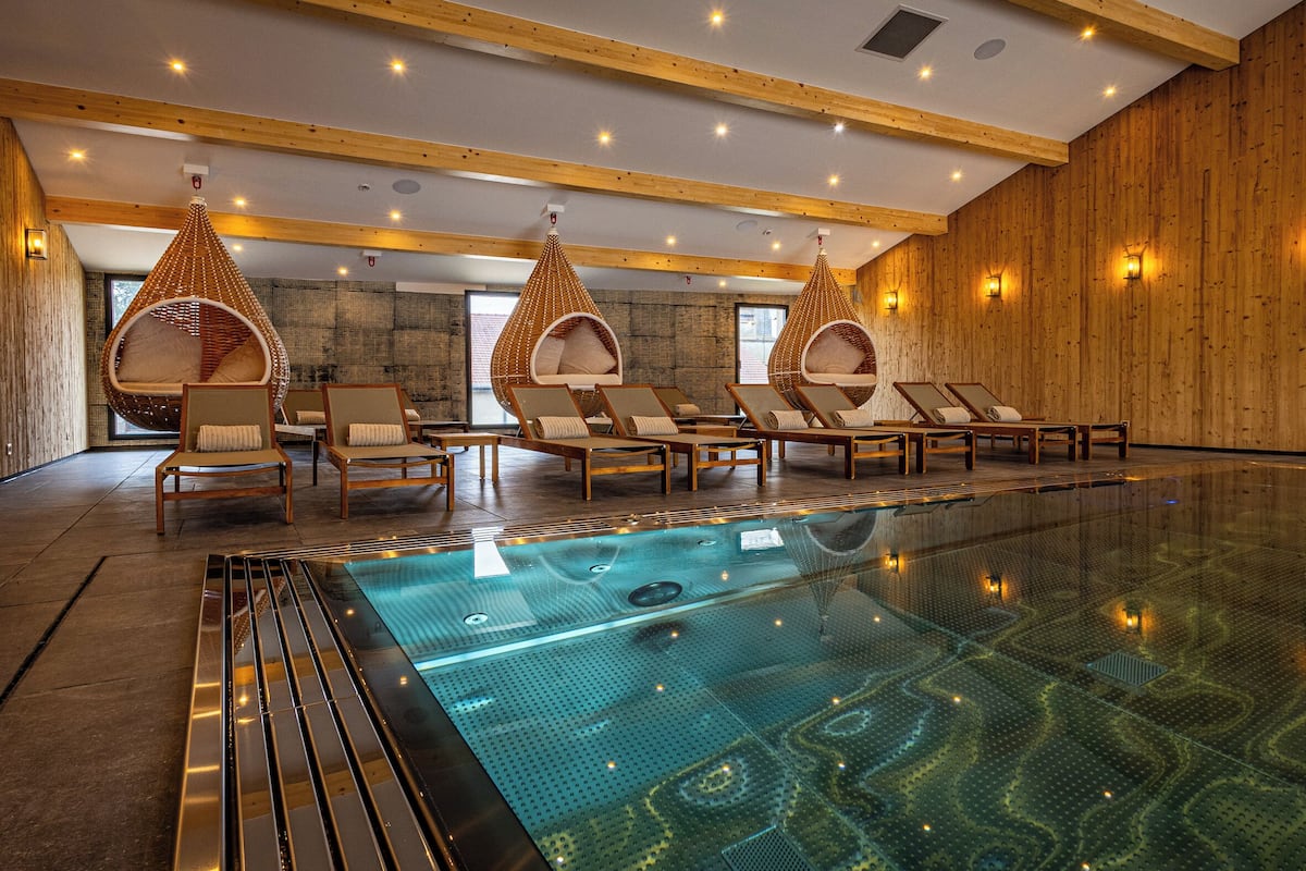 A modern indoor swimming pool with clear water, wooden walls, and lounge chairs.