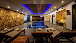 Un spa moderno con piscina climatizada, paneles de madera y zonas de relajación con sillas y toallas.