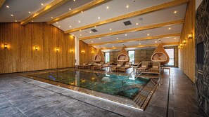 A large indoor swimming pool with wooden walls and ceiling, surrounded by lounge chairs and hanging chairs. - Hotel Restaurant Du Lac de Madine (Heudicourt-Sous-les-Cotes)