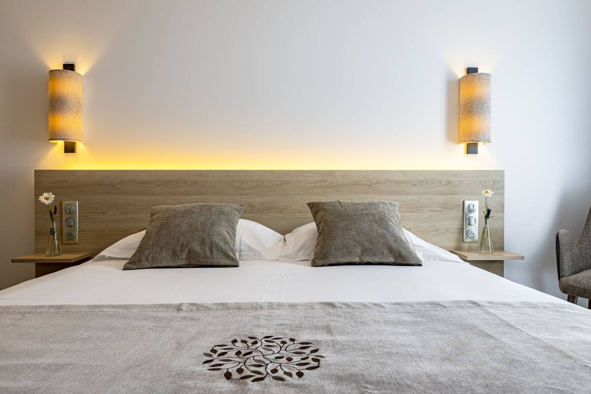 A neatly made bed with two pillows, a decorative throw, and a wooden headboard. There are two bedside tables with lamps and a small vase with flowers.