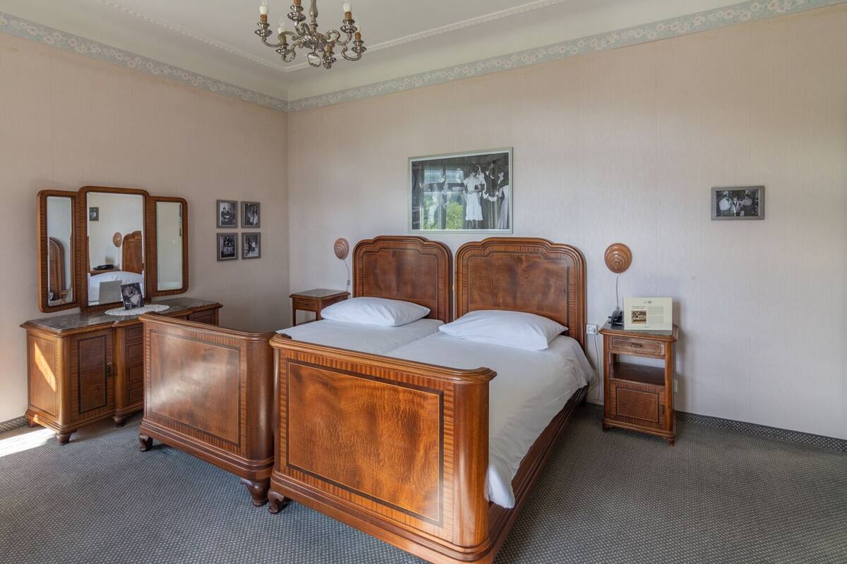 A hotel room with a large wooden bed, two nightstands, a dresser, and a chandelier.