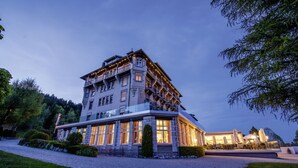 Un hôtel à plusieurs étages doté d’un balcon au dernier étage, d’une allée gravillonnée et d’un espace extérieur aménagé avec des parasols.