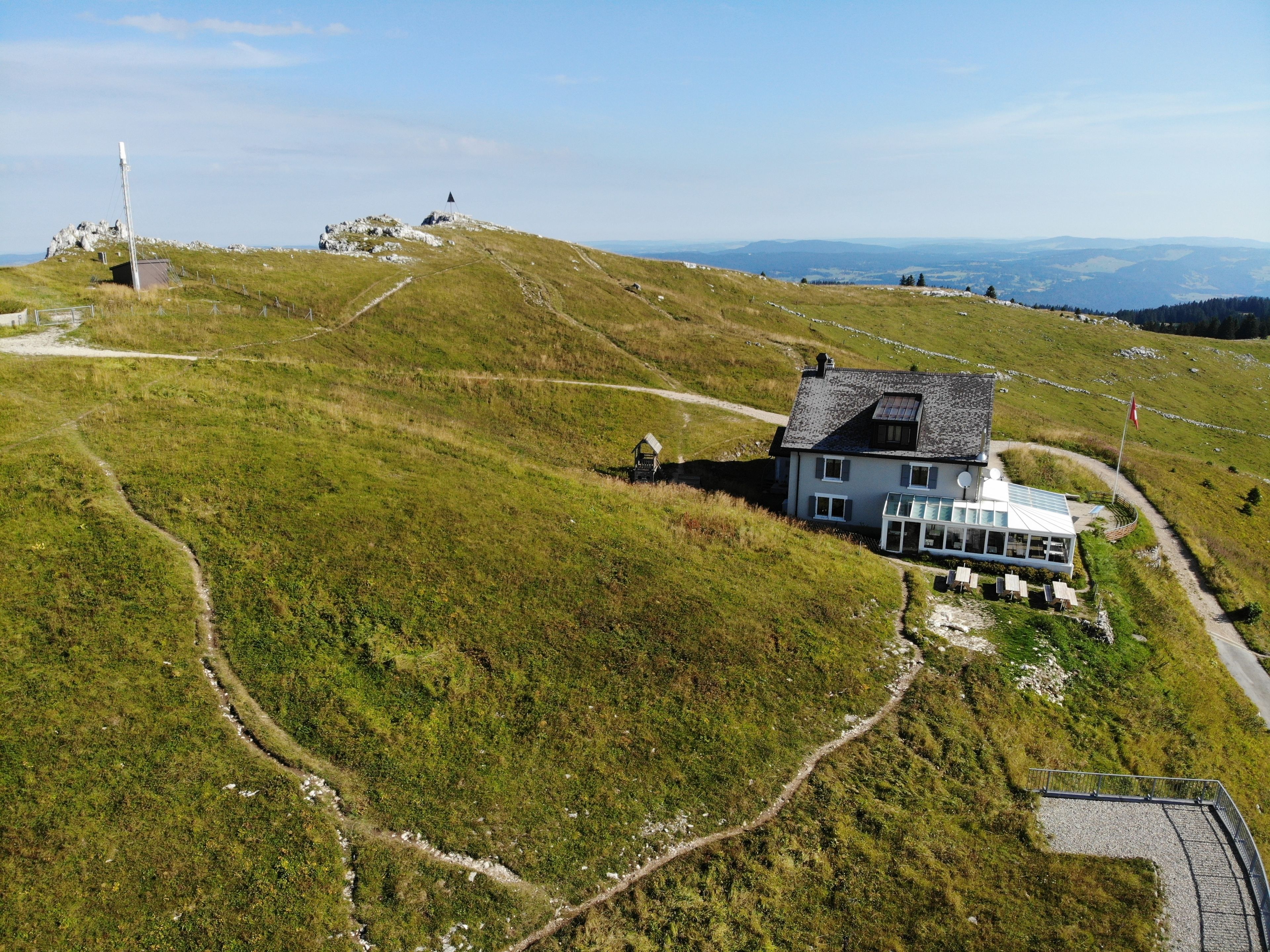 Uma casa com telhado inclinado, cercada por um muro, e vista ampla da paisagem.