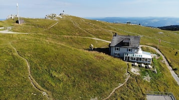 Uma casa com telhado inclinado, cercada por um muro, e vista ampla da paisagem.