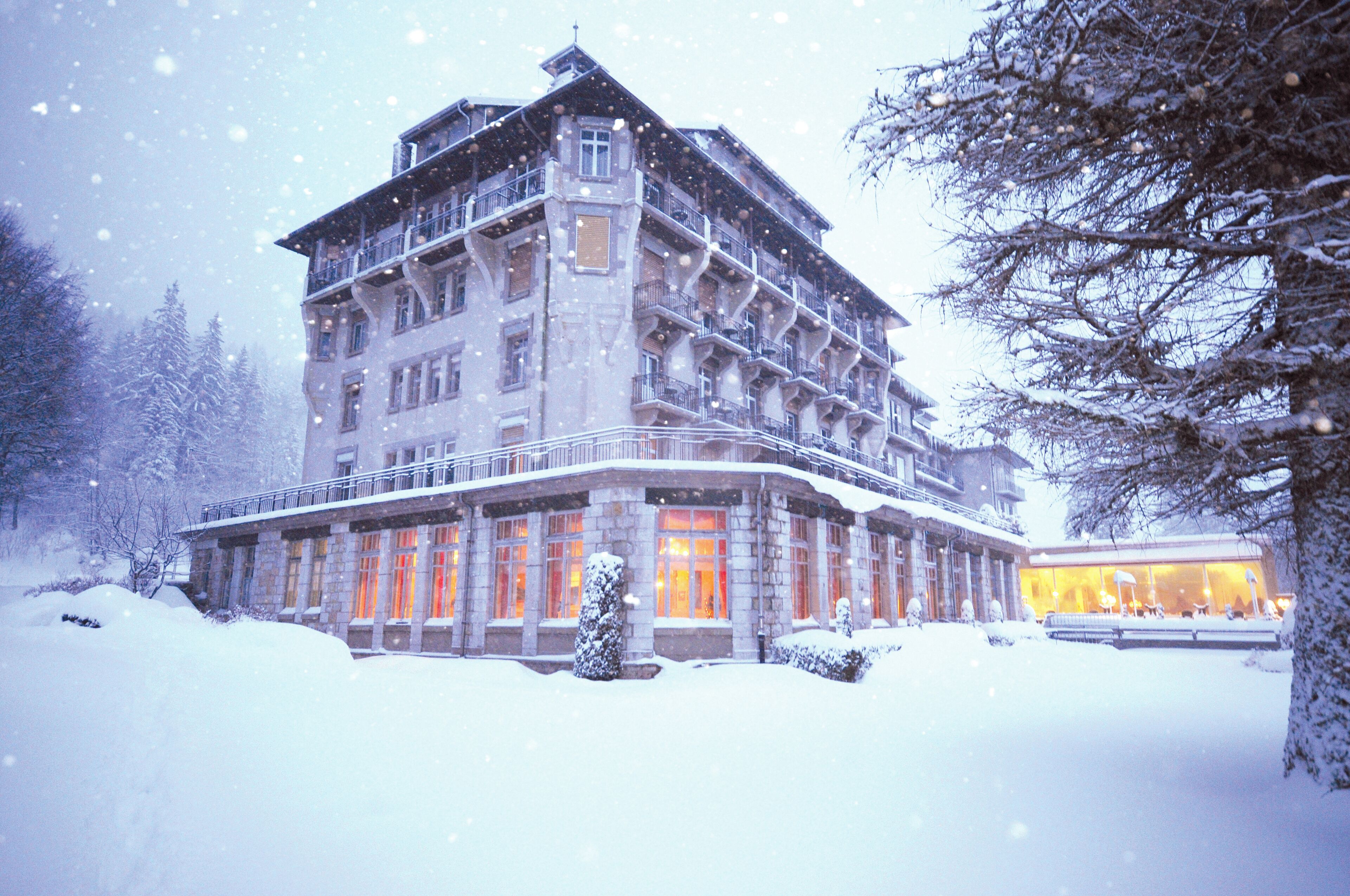 Un hotel de varios pisos con un balcón en el segundo nivel, rodeado de árboles cubiertos de nieve.