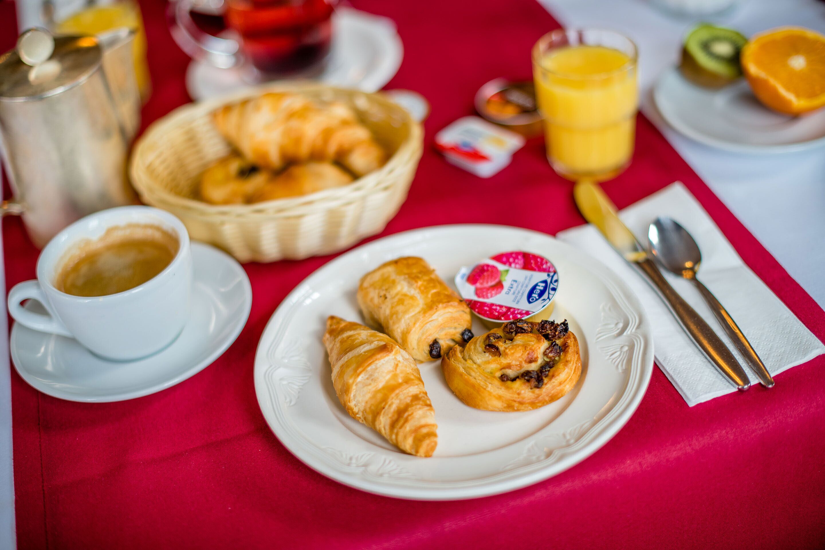 Une table dressée pour le petit-déjeuner avec des croissants, une tasse de café, un verre de jus d’orange et un panier de pain.