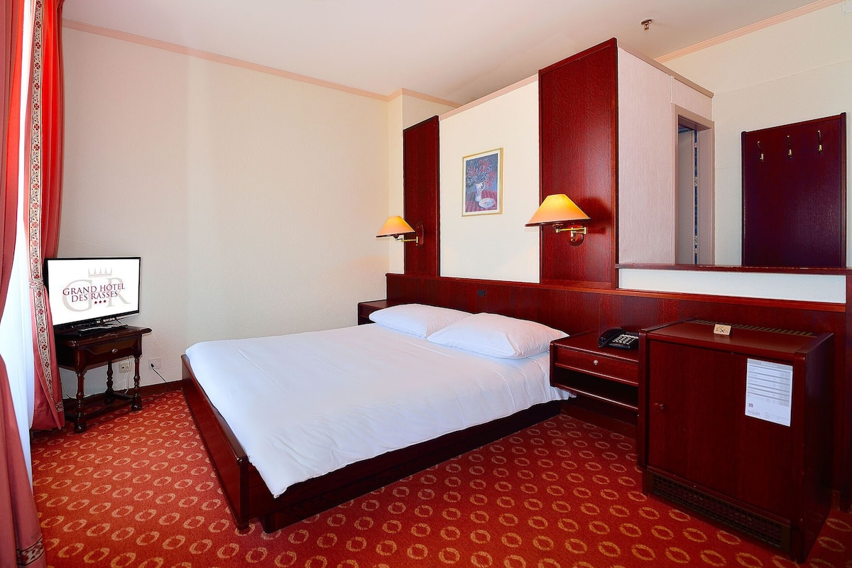 A hotel room with a bed, a desk with a lamp, a television, and a mirror.