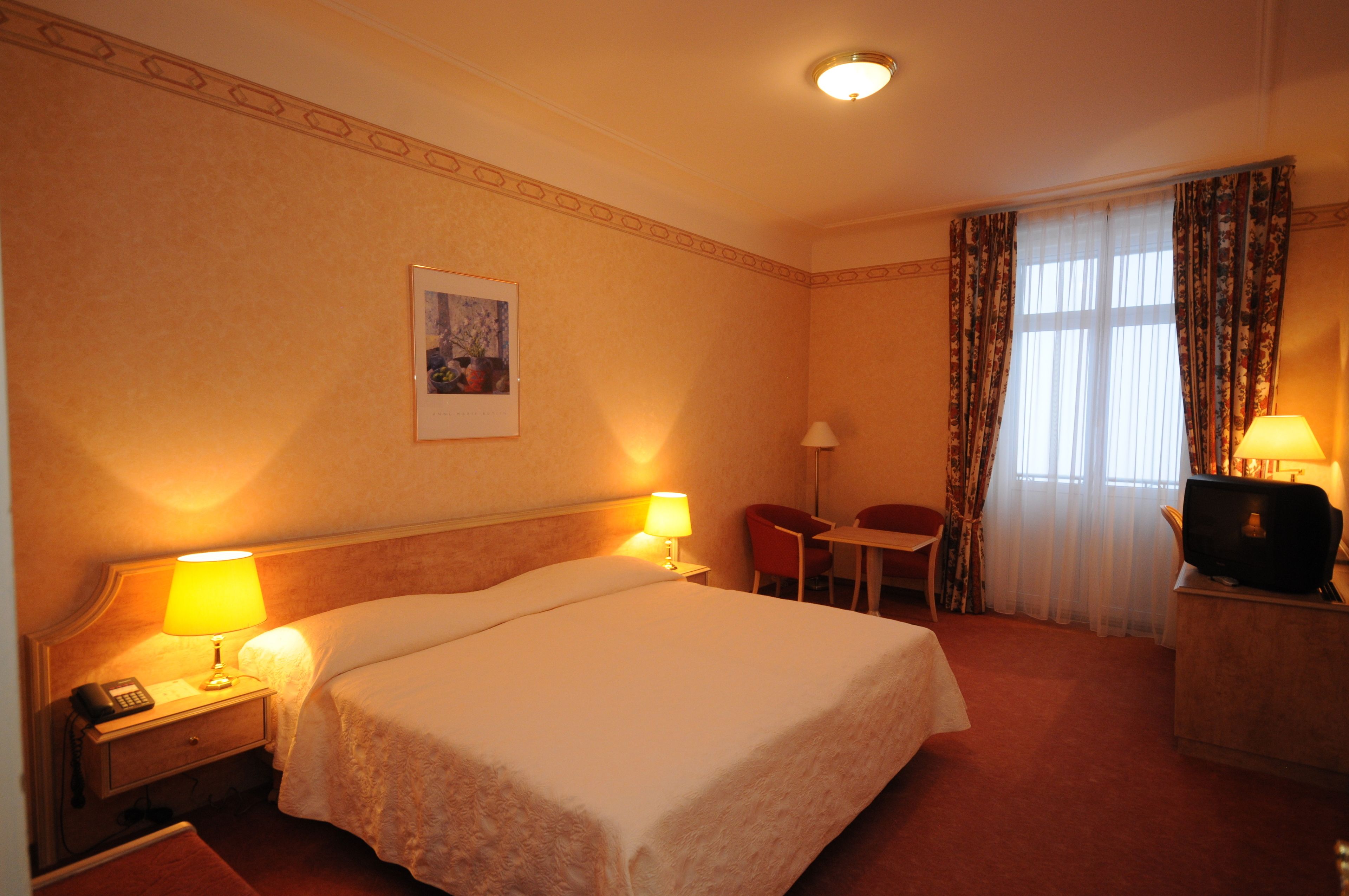 A hotel room with a large bed, bedside lamps, a desk with a television, and a chair.
