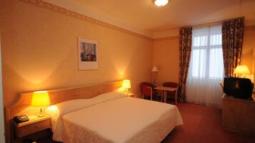 A hotel room with a large bed, bedside lamps, a desk with a television, and a chair.