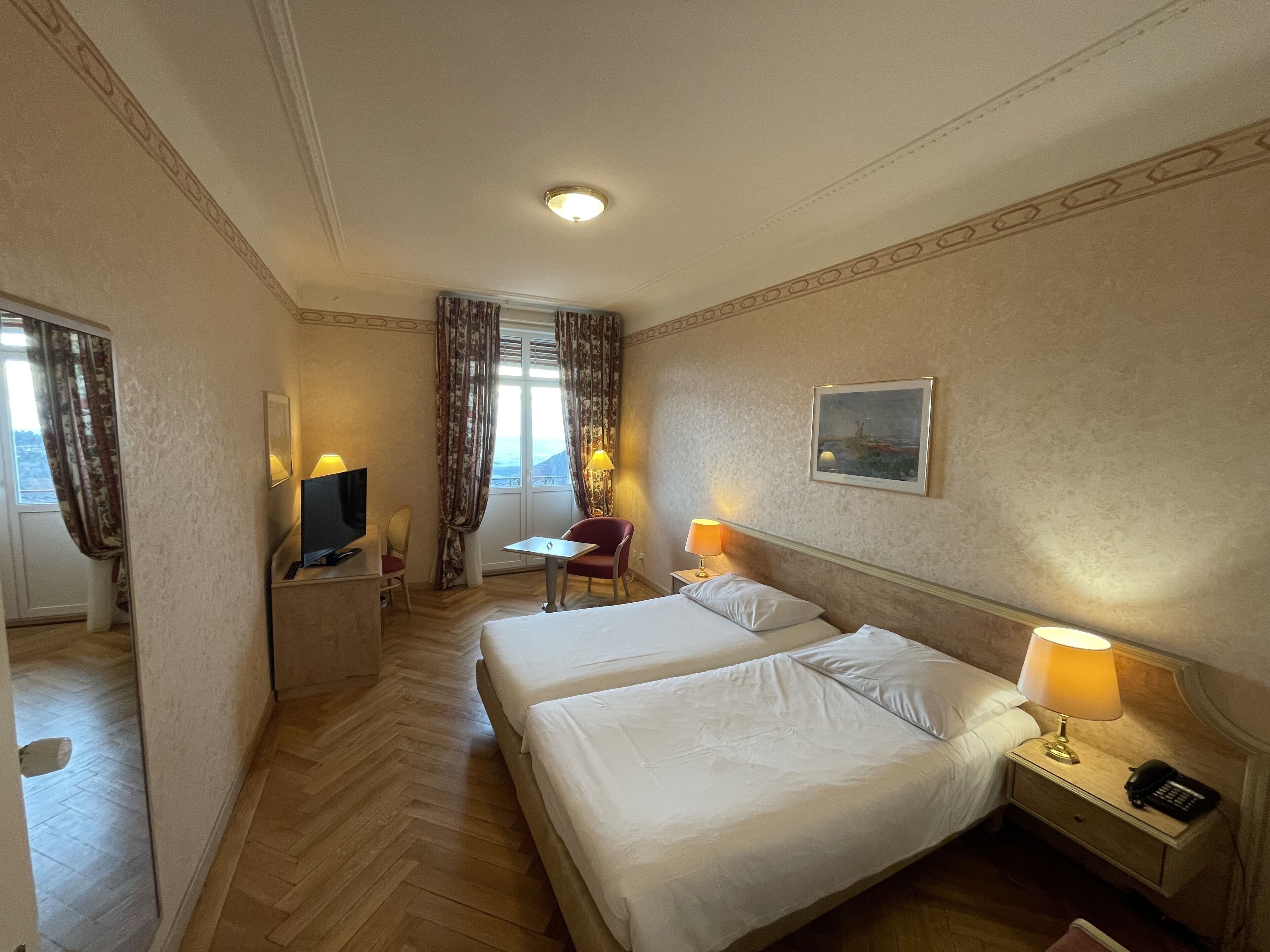 Une chambre d’hôtel avec deux lits, un bureau avec une chaise, une télévision et un tableau au mur.