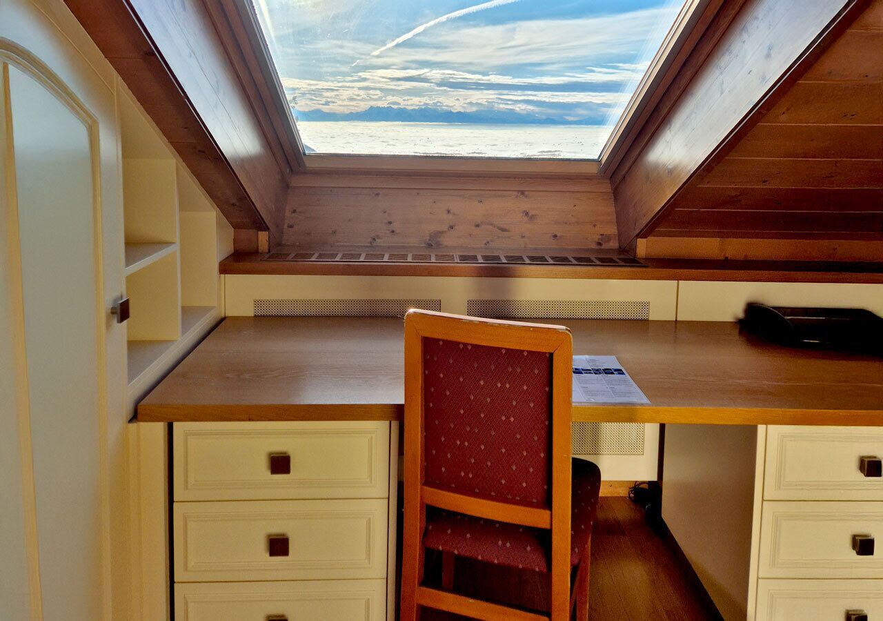 A room with a wooden desk, a chair, and a skylight.