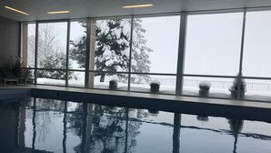 Une piscine intérieure avec de grandes fenêtres donnant sur des arbres couverts de neige.