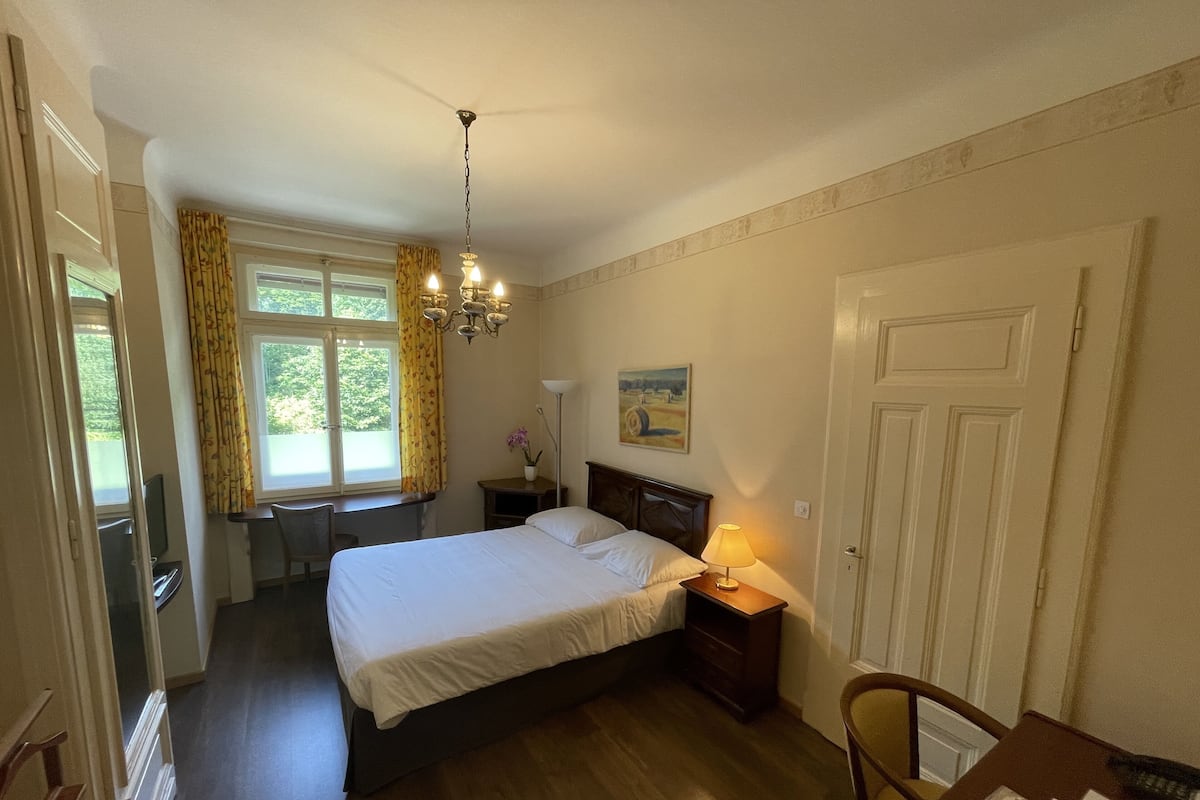 A bedroom with a bed, bedside table, lamp, and a window with curtains.