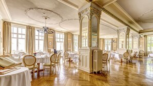 Une salle à manger spacieuse dotée d’un parquet en bois, de tables blanches et de chaises en osier.