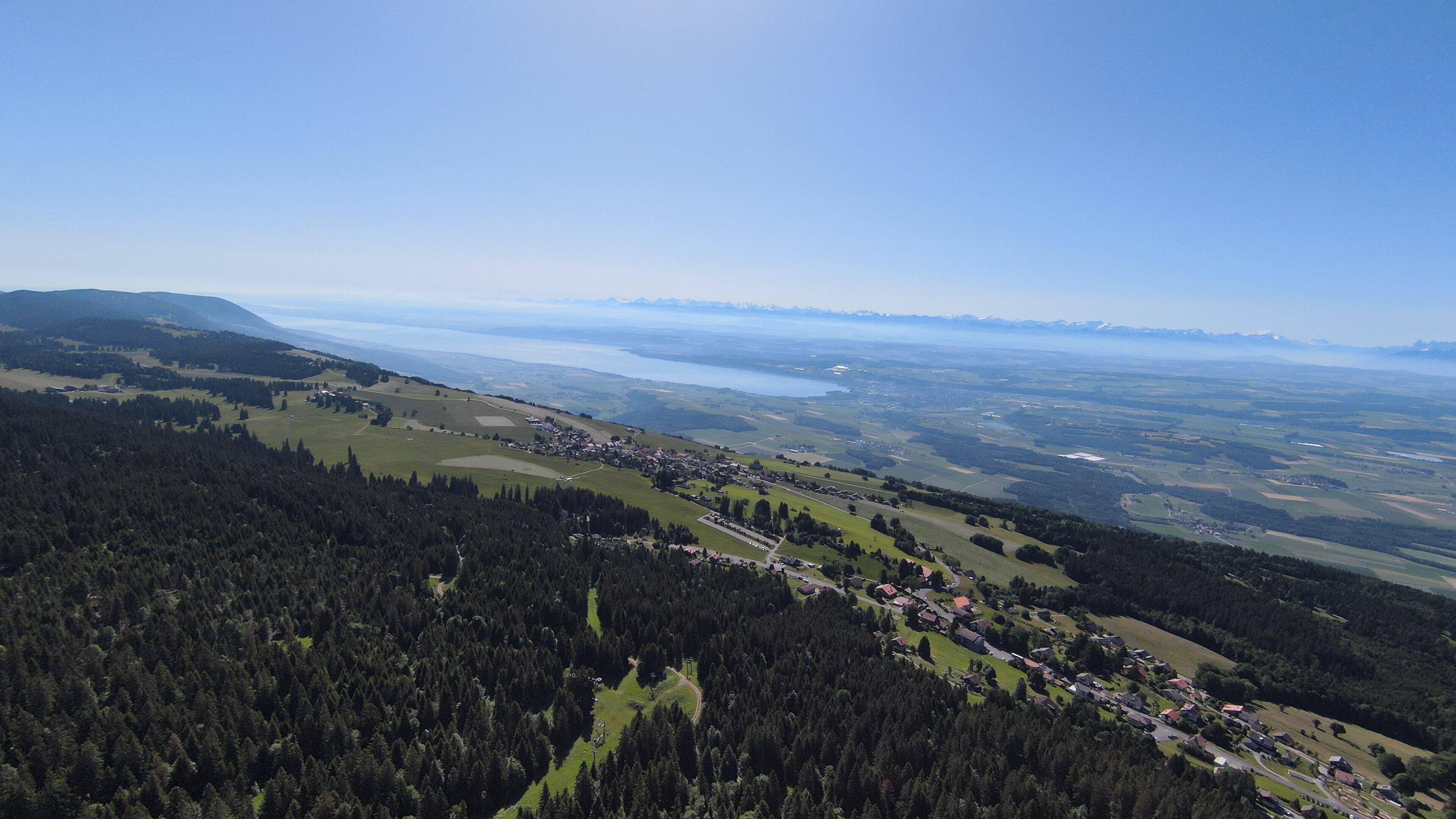 Une vue panoramique d’une ville entourée de forêts et de collines, avec un lac à l’horizon.