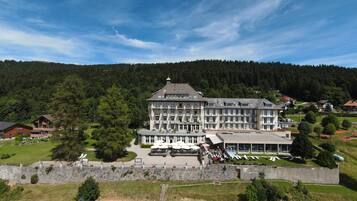 A large, multi-story hotel with a central courtyard, surrounded by lush greenery and a forested hillside.