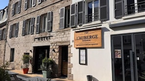 Un hôtel avec une façade en pierre, une enseigne en bois et une entrée bien visible.