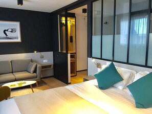 Et moderne hotelværelse med seng, sofa, et lille bord og et spejl.