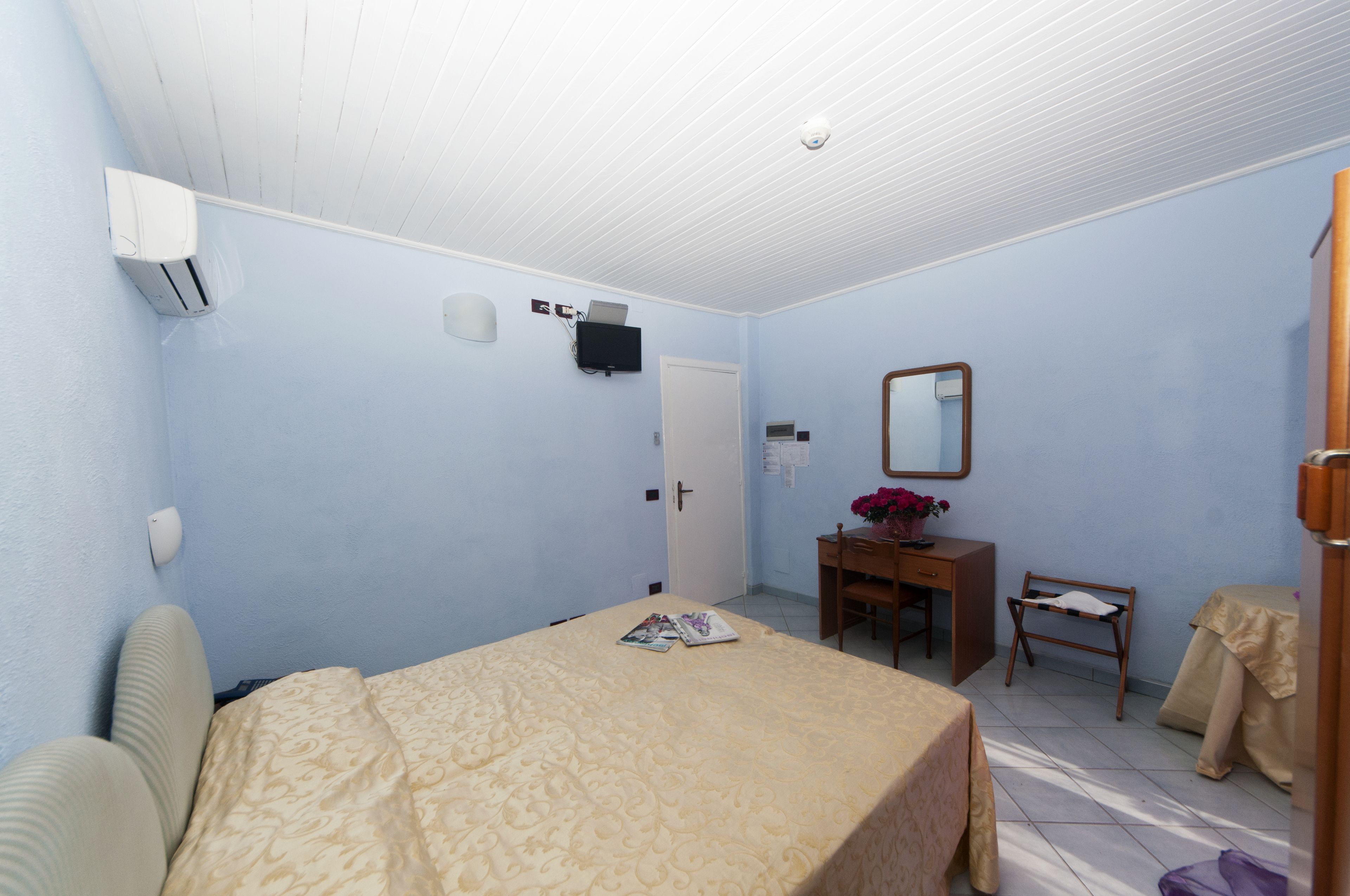 Una habitación con cama, escritorio, silla, espejo y puerta.