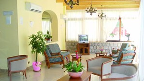 Un salón amplio con diversas opciones de asientos, un televisor y plantas decorativas.