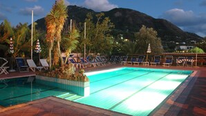 Una piscina con sillas de descanso y palmeras, rodeada de montañas.