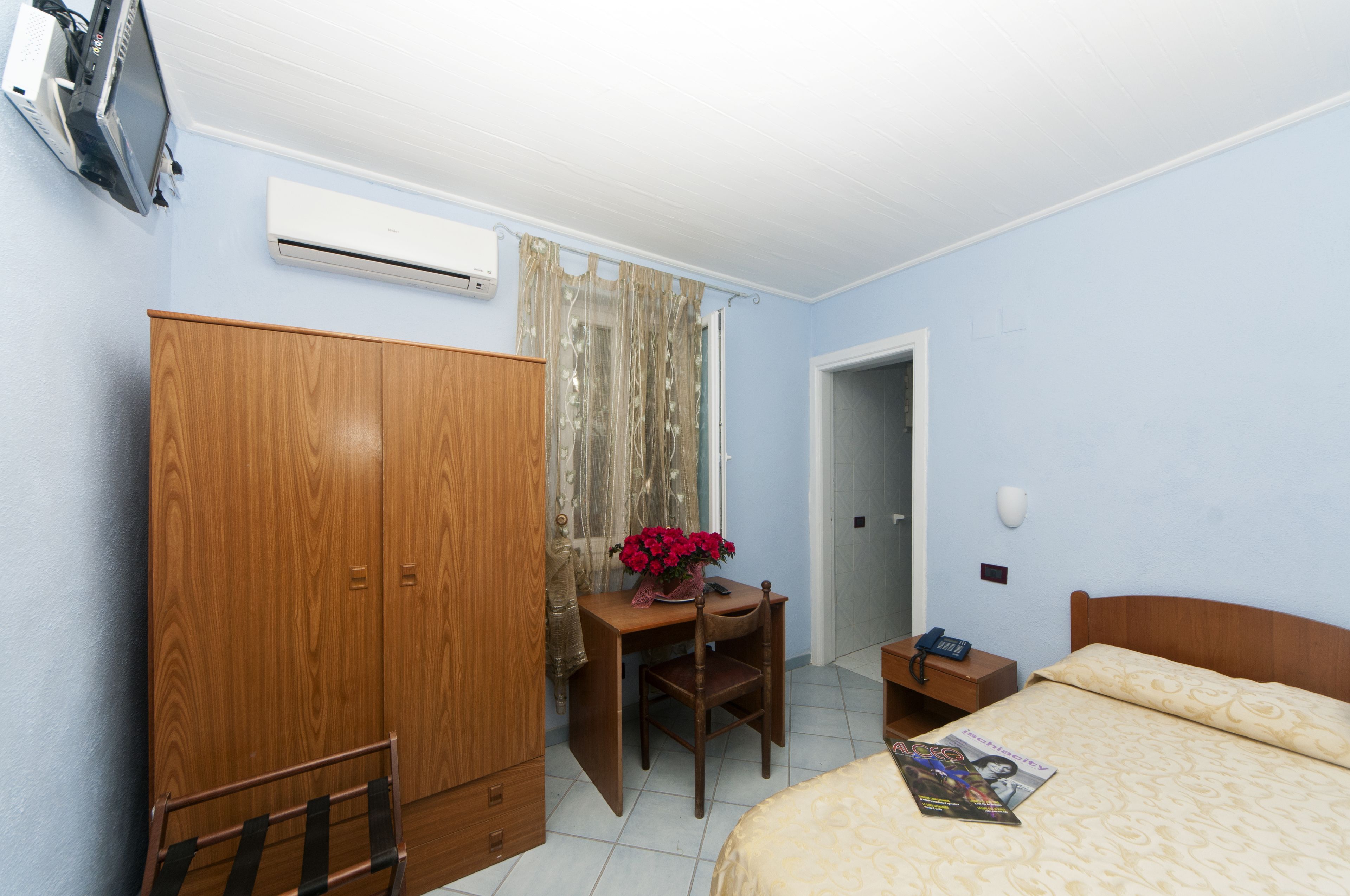 Un dormitorio con cama, armario de madera, escritorio con silla y una mesita con teléfono.