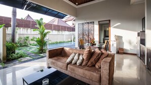 Un salon moderne avec un canapé marron, une table basse en verre et une vue sur une piscine et un jardin.