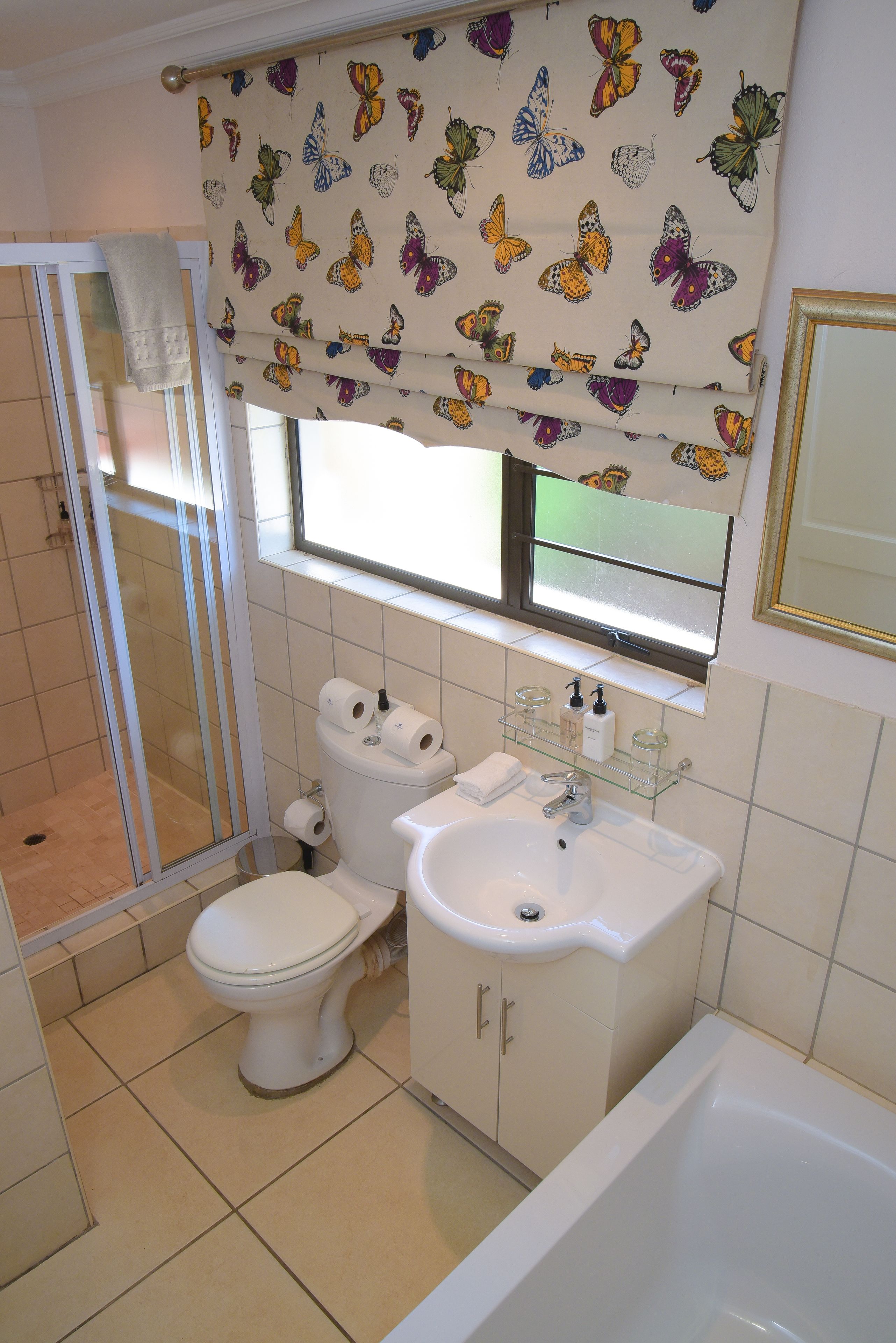 A bathroom with a toilet, sink, and bathtub. There is a window with butterfly-patterned curtains.