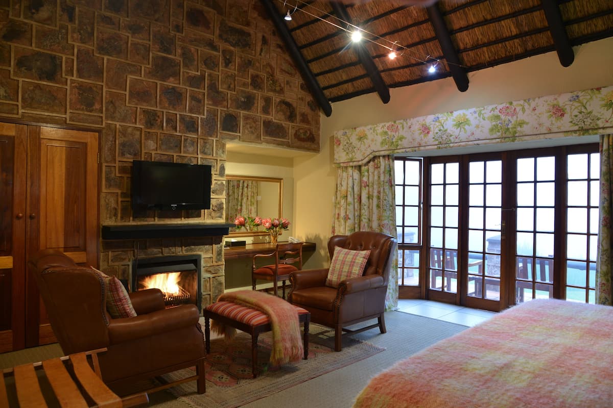 A cozy room with a stone fireplace, leather armchairs, a television, and a balcony with large windows.