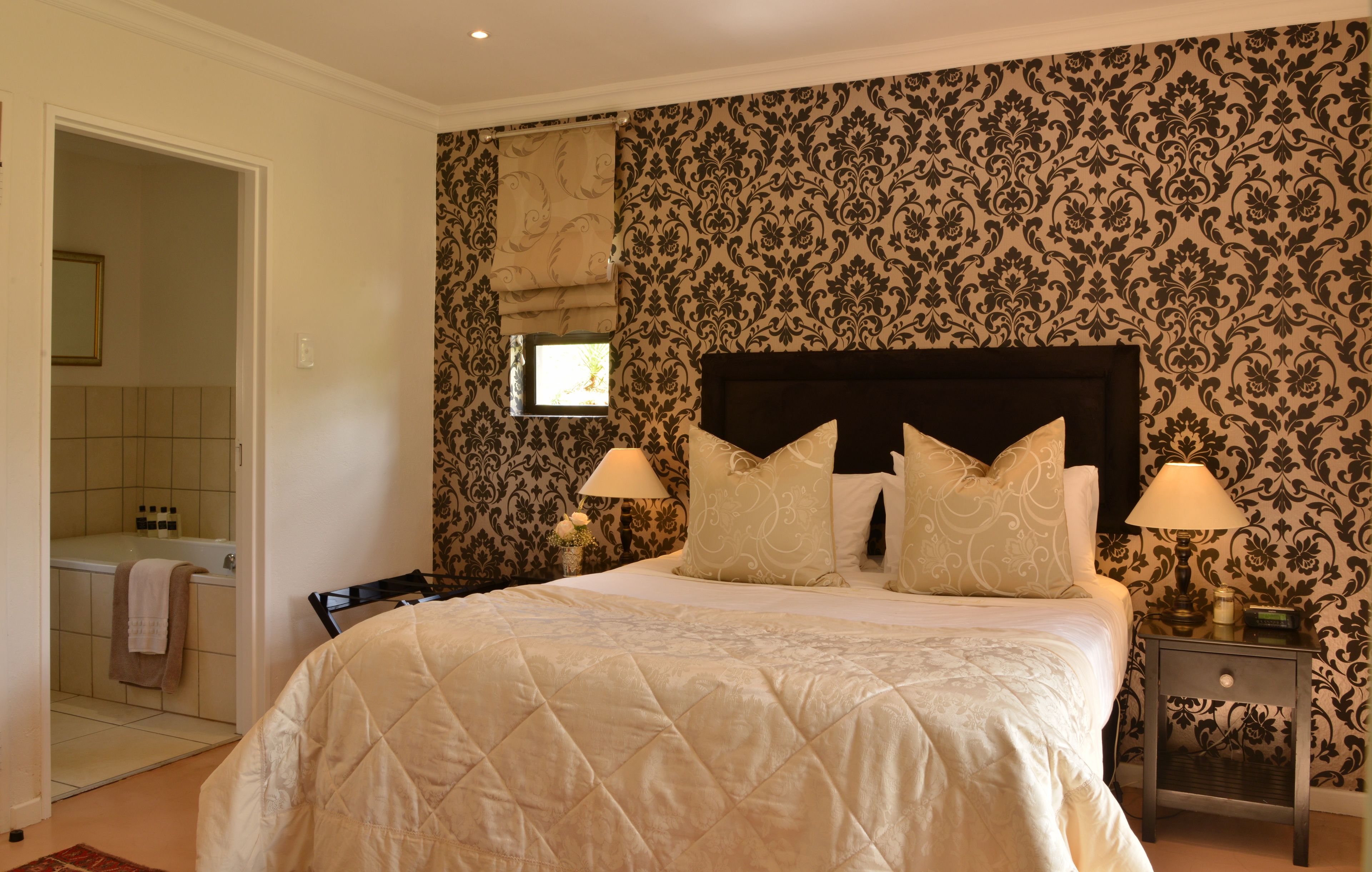 Een slaapkamer met een groot bed, twee bedlampen, een nachtkastje, een raam met uitzicht, en een zichtbare badkamer door een geopende deur.