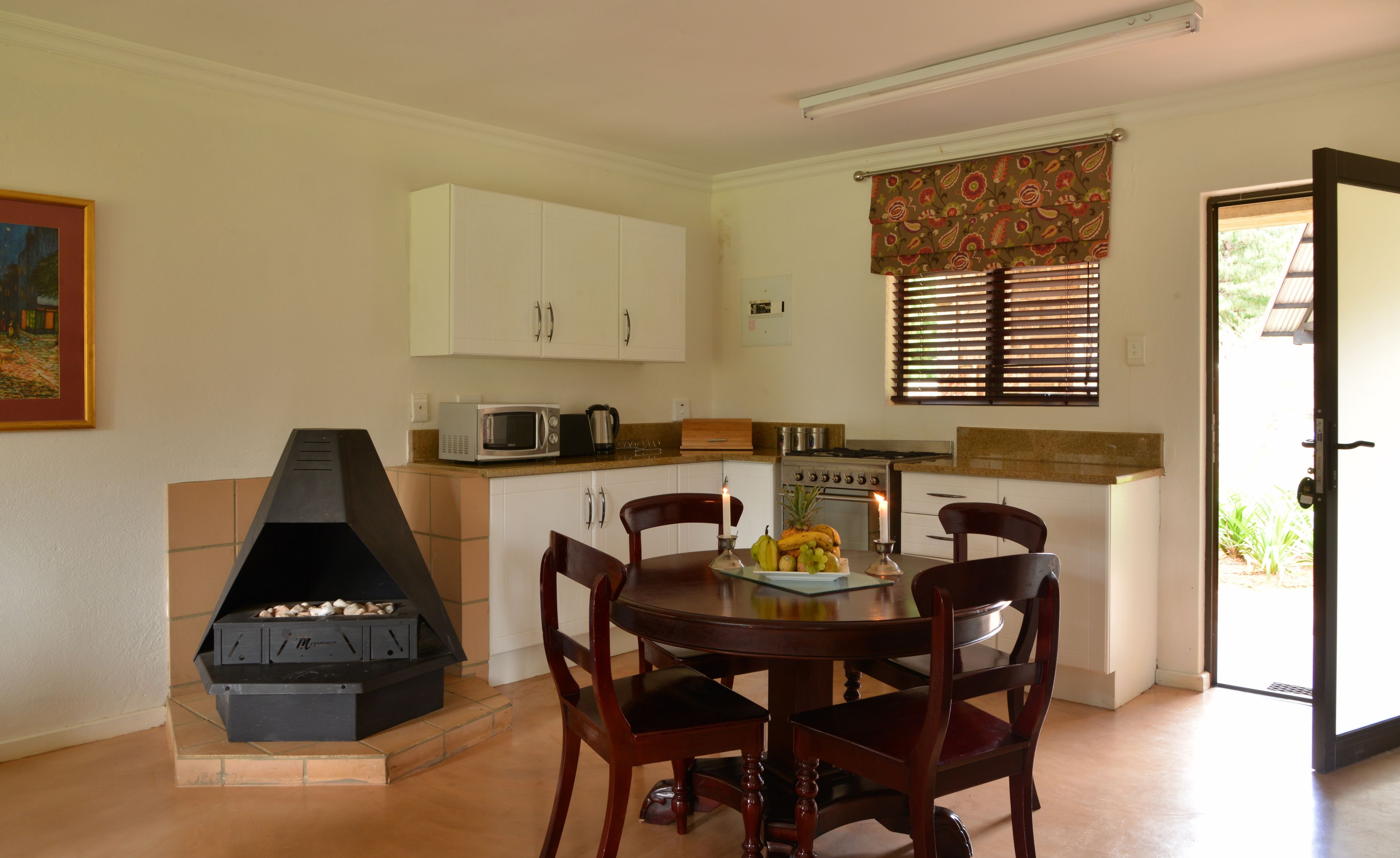 Una cocina compacta con armarios blancos, un microondas, una estufa y una mesa de comedor con sillas.