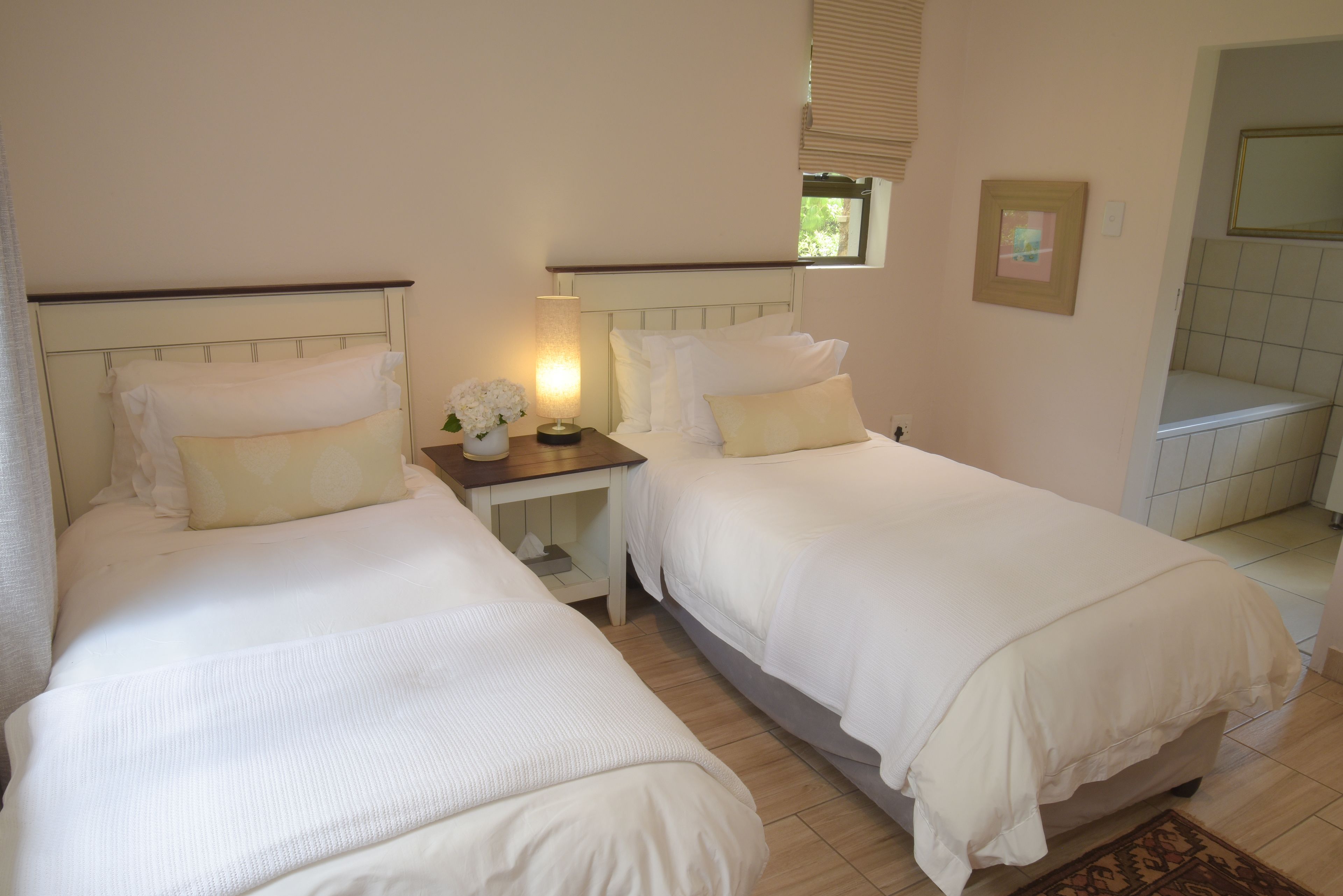 Una habitación de hotel con dos camas, una mesita de noche con lámpara y una ventana con persianas.